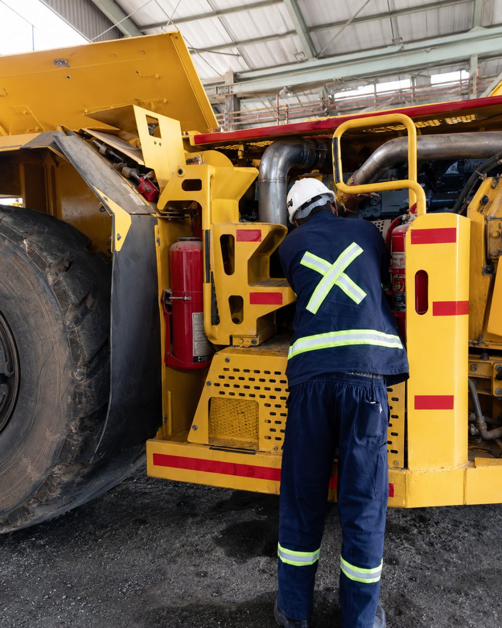 Technician in protective clothing working on the engine bay of an underground loader inside the workshop.
